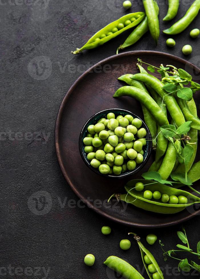 Guisantes en un tazón con vainas frescas sobre el fondo de hormigón negro, vista superior o endecha plana foto