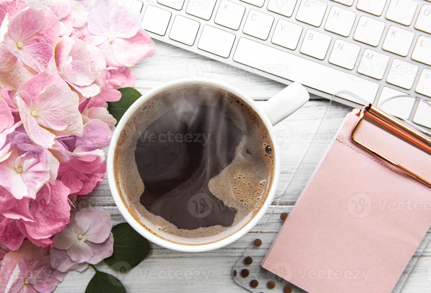 Home office desk workspace with pink hydrangea flower bouquet, cup of coffee and keyboard photo