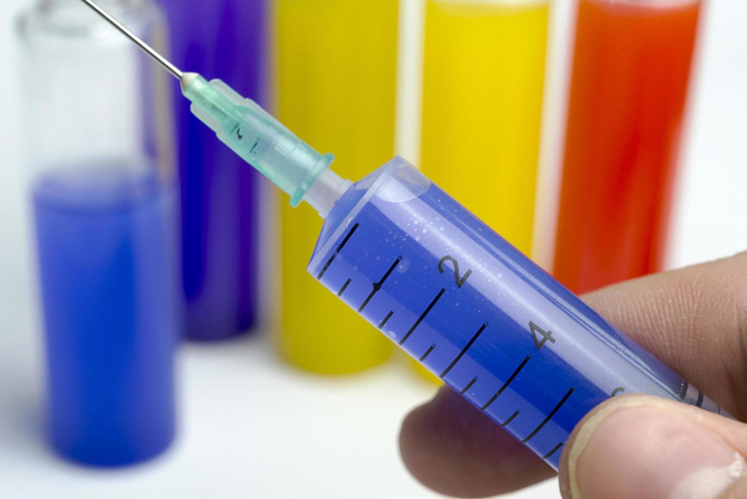 Hand holding test tube with blue liquid and a syringe. photo