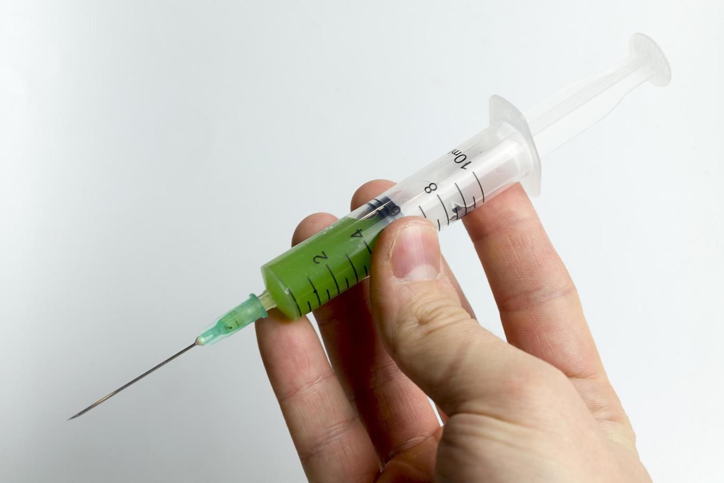 A hand holding a syringe with green liquid. photo
