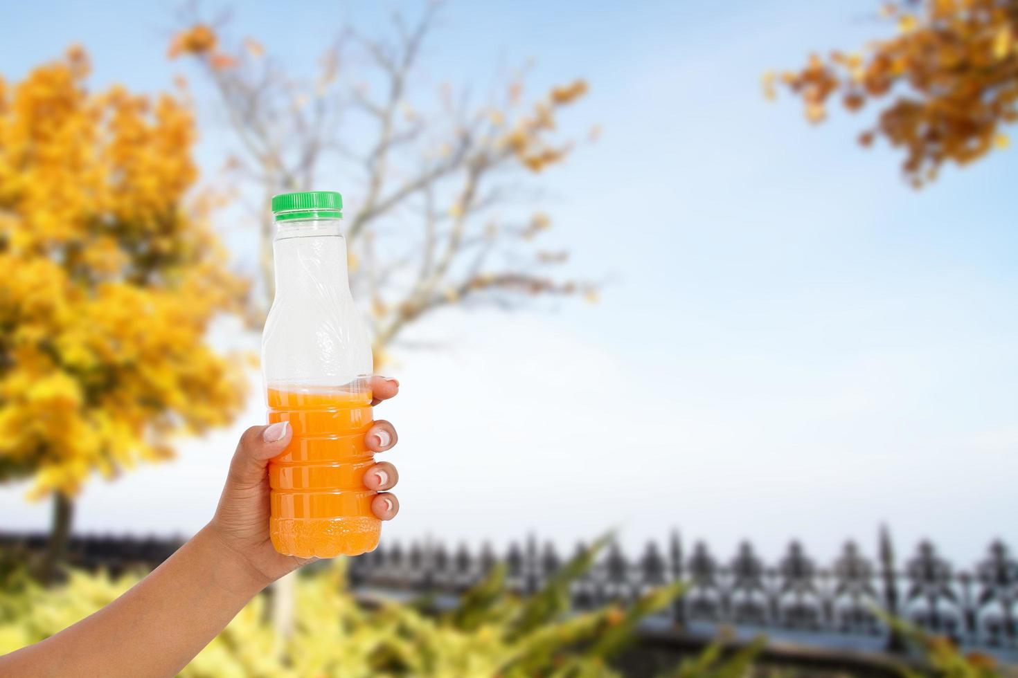black womans hand hold juice bottle on blurred park background, healthy lifestyle concept photo