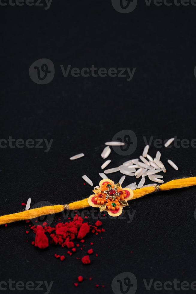 Raksha Bandhan Rakhi with rice grains and kumkum on black background, Traditional Indian wrist band which is a symbol of love between Brothers and Sisters. photo