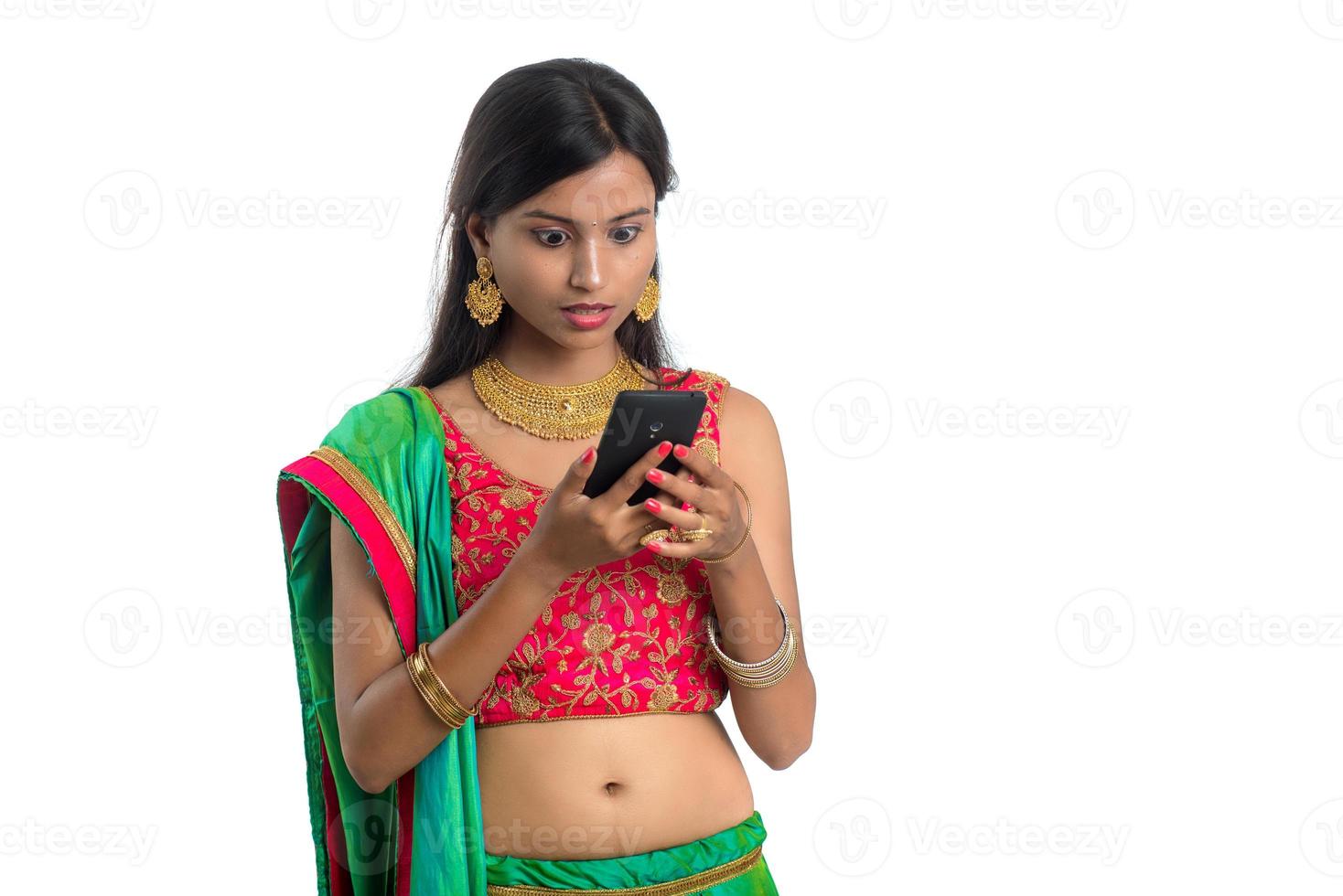 Young Indian traditional girl using a mobile phone or smartphone isolated on a white background photo