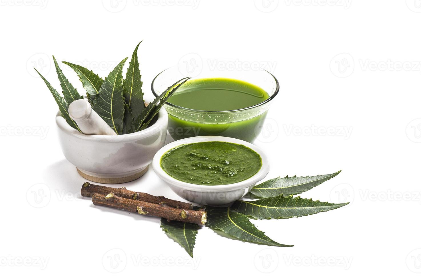 Medicinal Neem leaves in mortar and pestle with neem paste, juice and twigs on white background photo