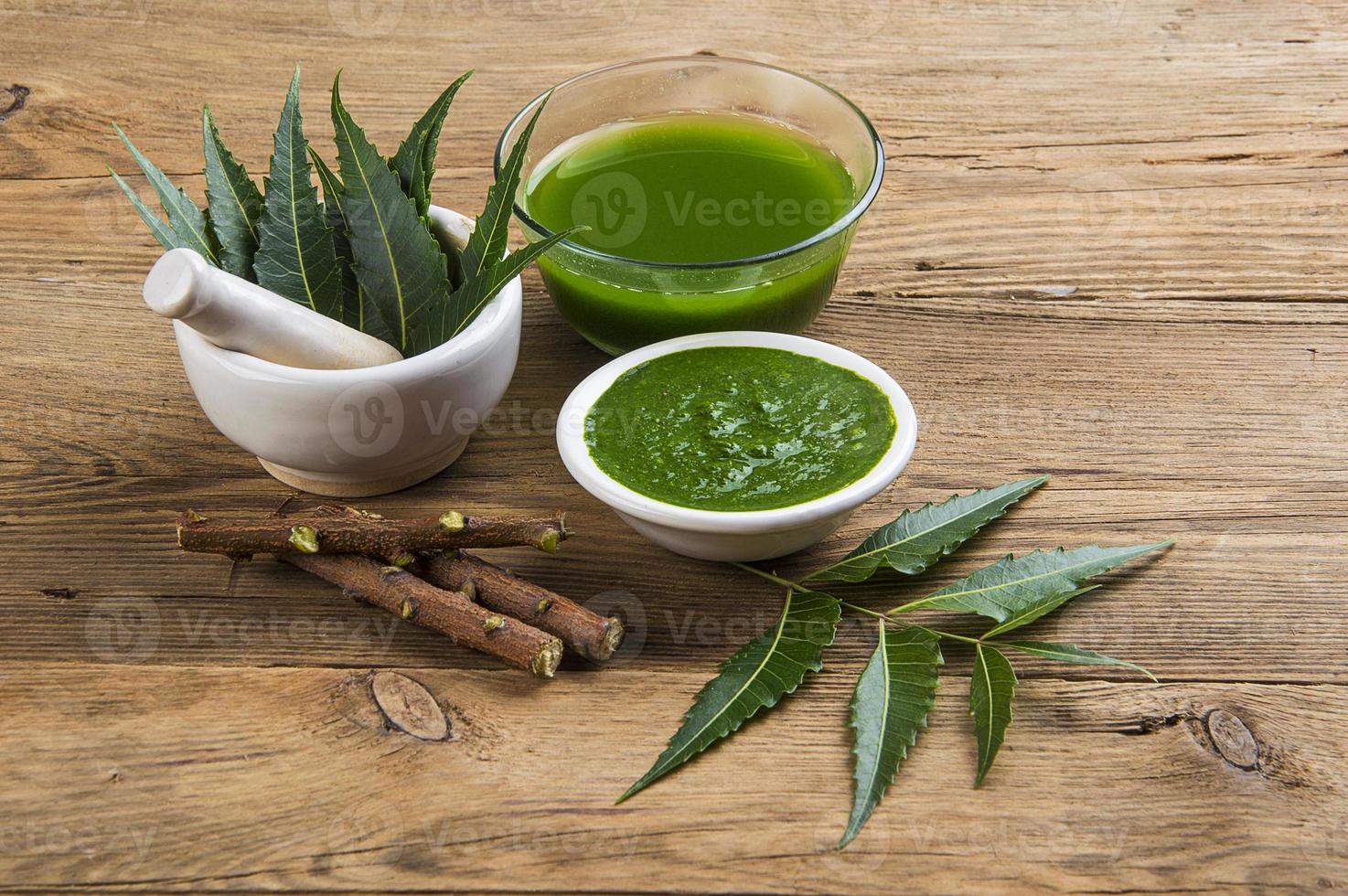 Medicinal Neem leaves in mortar and pestle with neem paste, juice and twigs on wooden background photo