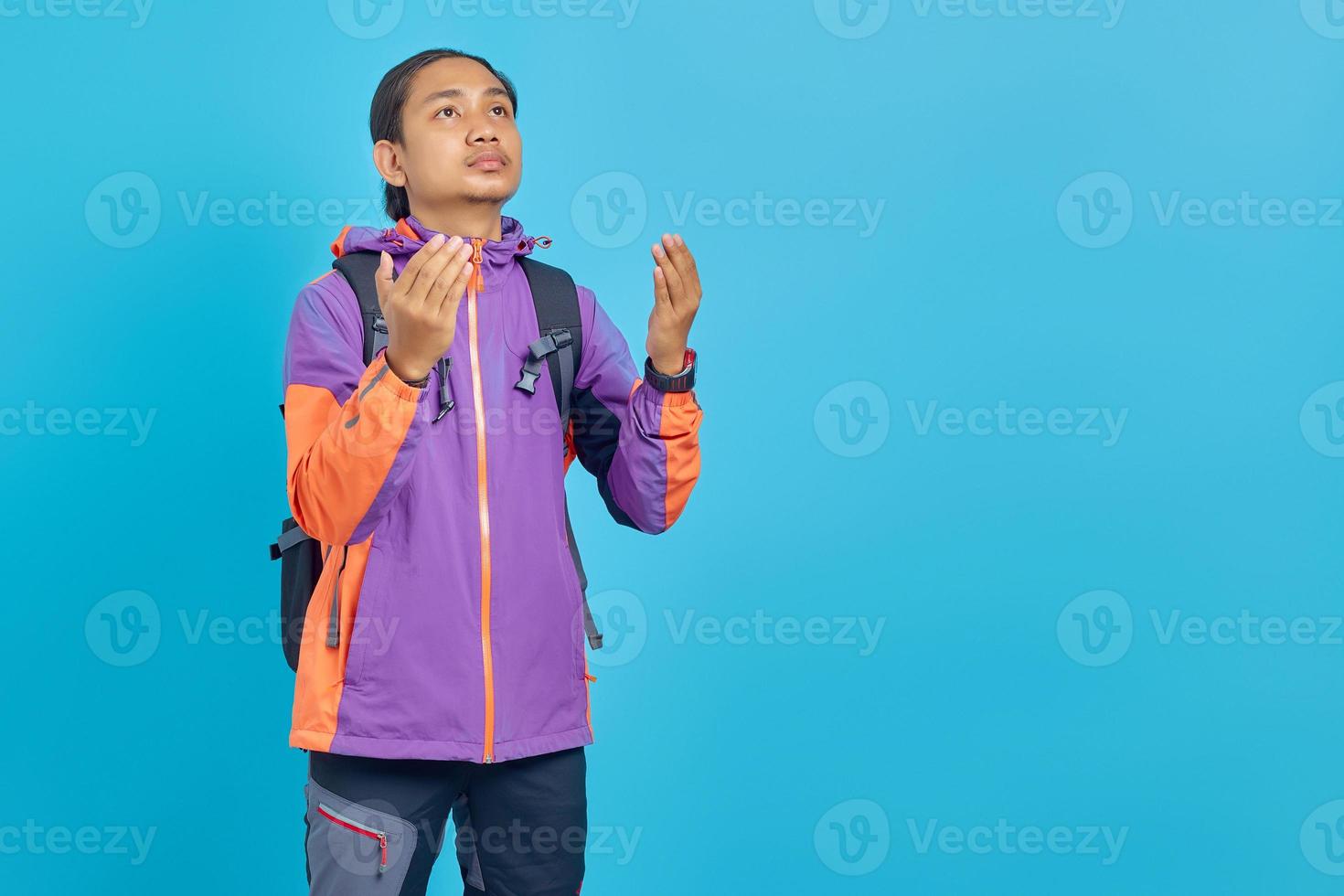 Retrato de joven asiática rezando mientras sostiene las palmas hacia arriba aislado sobre fondo azul. foto