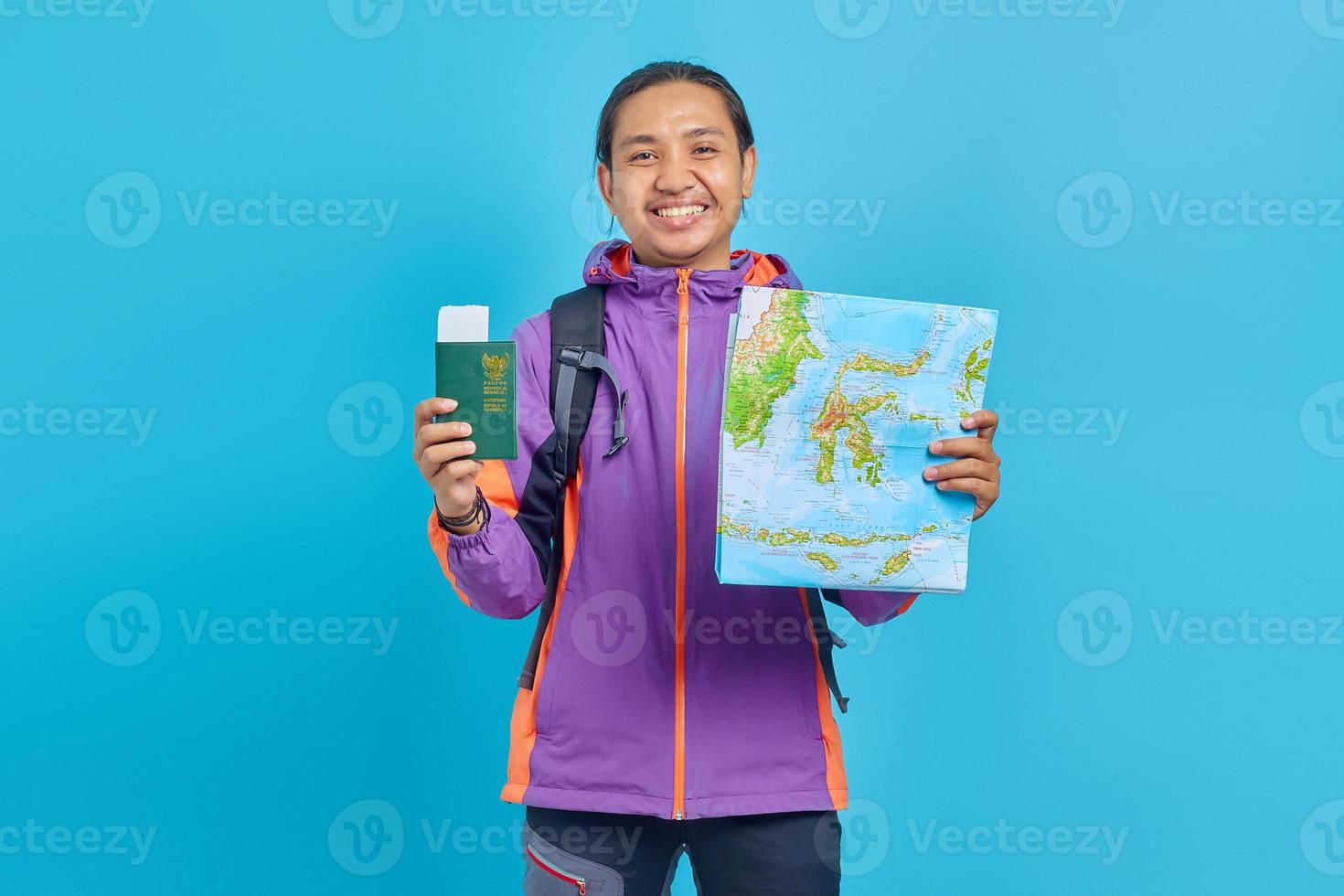 retrato, de, alegre, asiático, joven, llevando, chaqueta púrpura, actuación, mapa, y, pasaporte, libro, aislado, en, fondo azul foto
