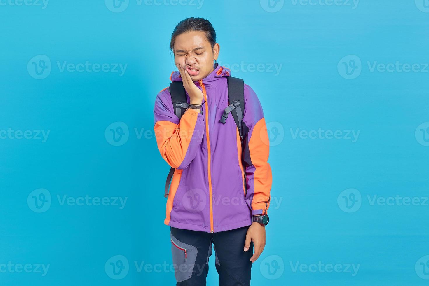 Portrait of handsome Asian man having toothache with painful expression and touching mouth on blue background photo