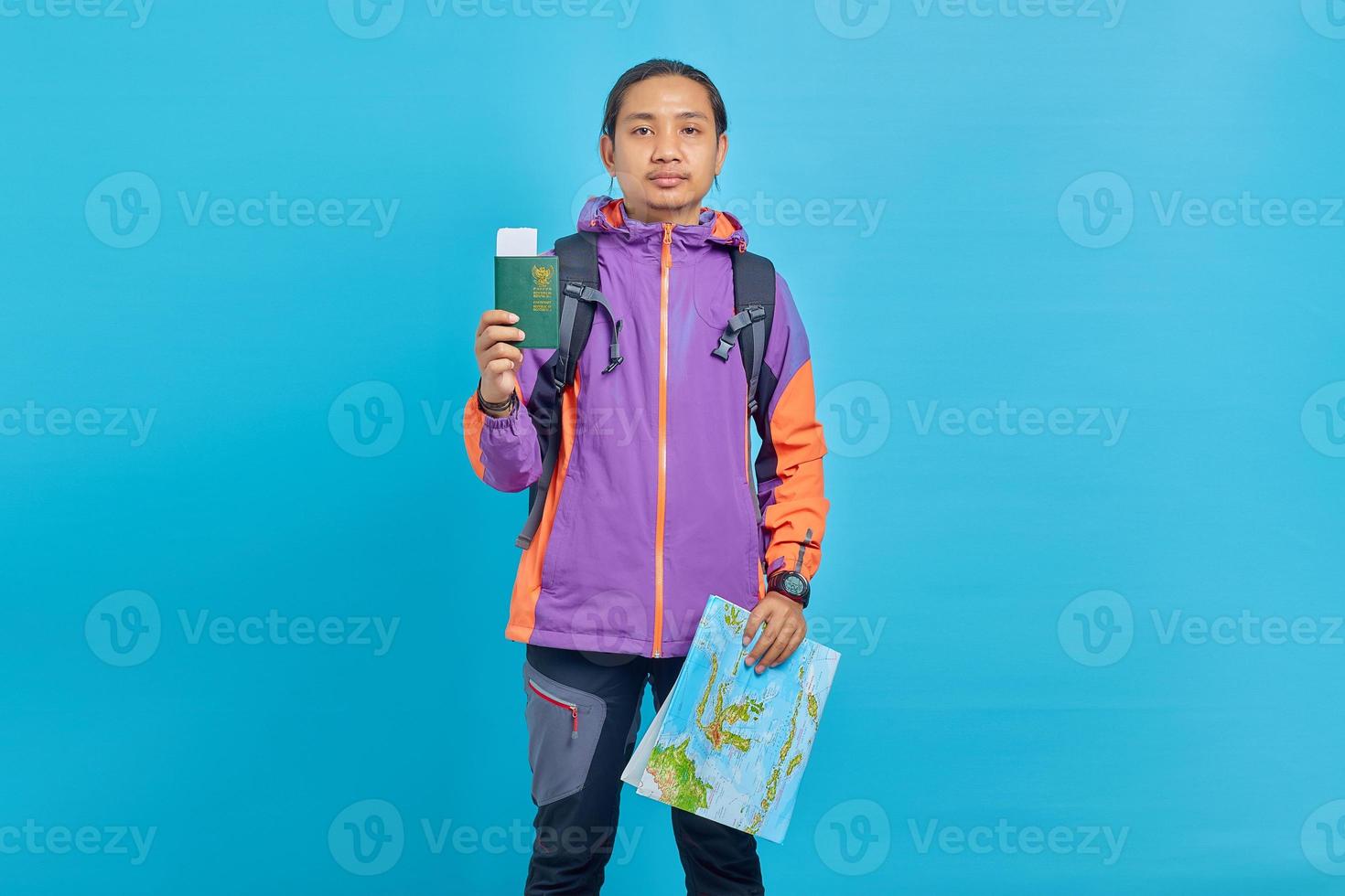 retrato, de, alegre, asiático, joven, llevando, chaqueta púrpura, actuación, mapa, y, pasaporte, libro, aislado, en, fondo azul foto