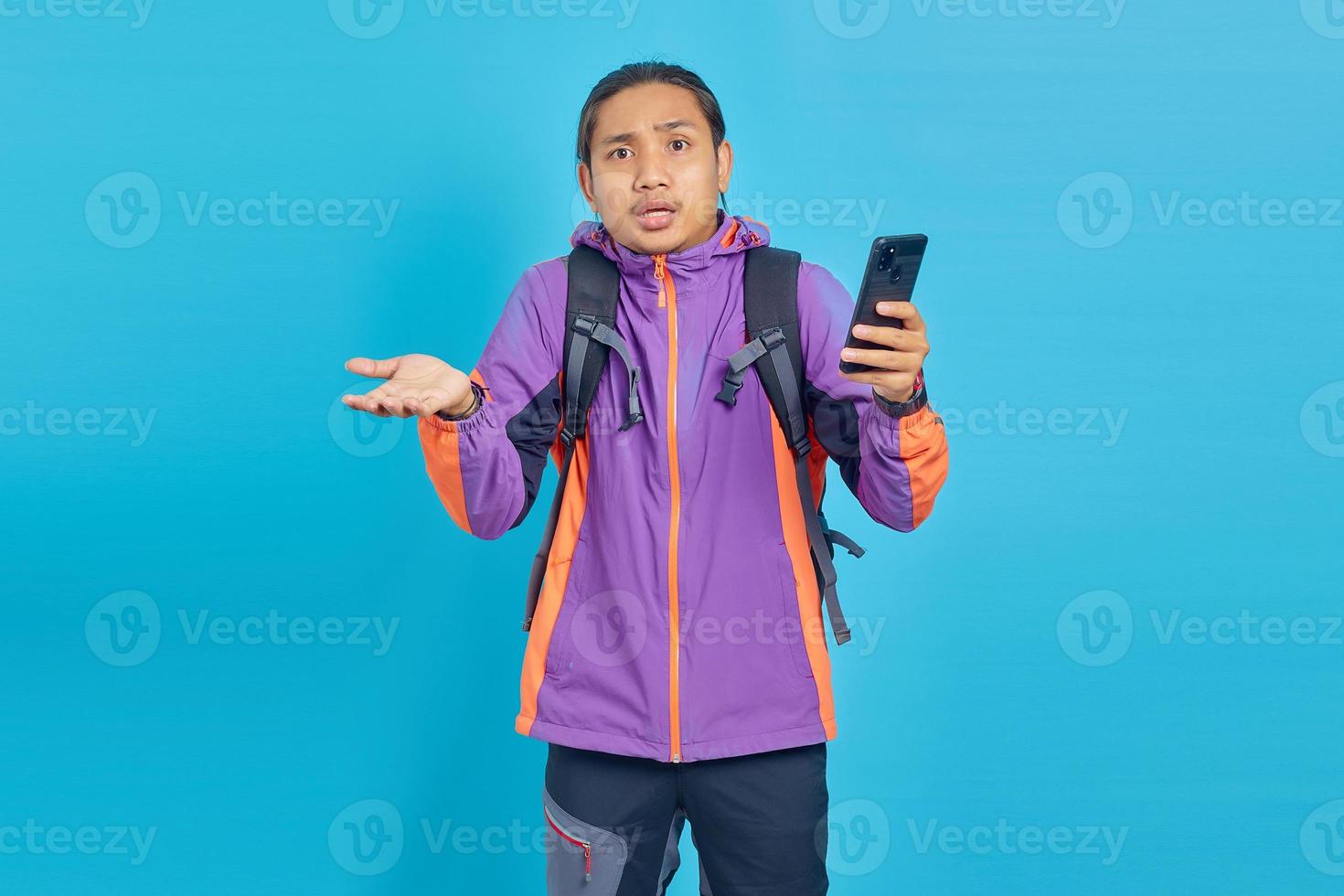 Portrait of surprised young Asian man holding on mobile phone with open mouth isolated on blue background photo