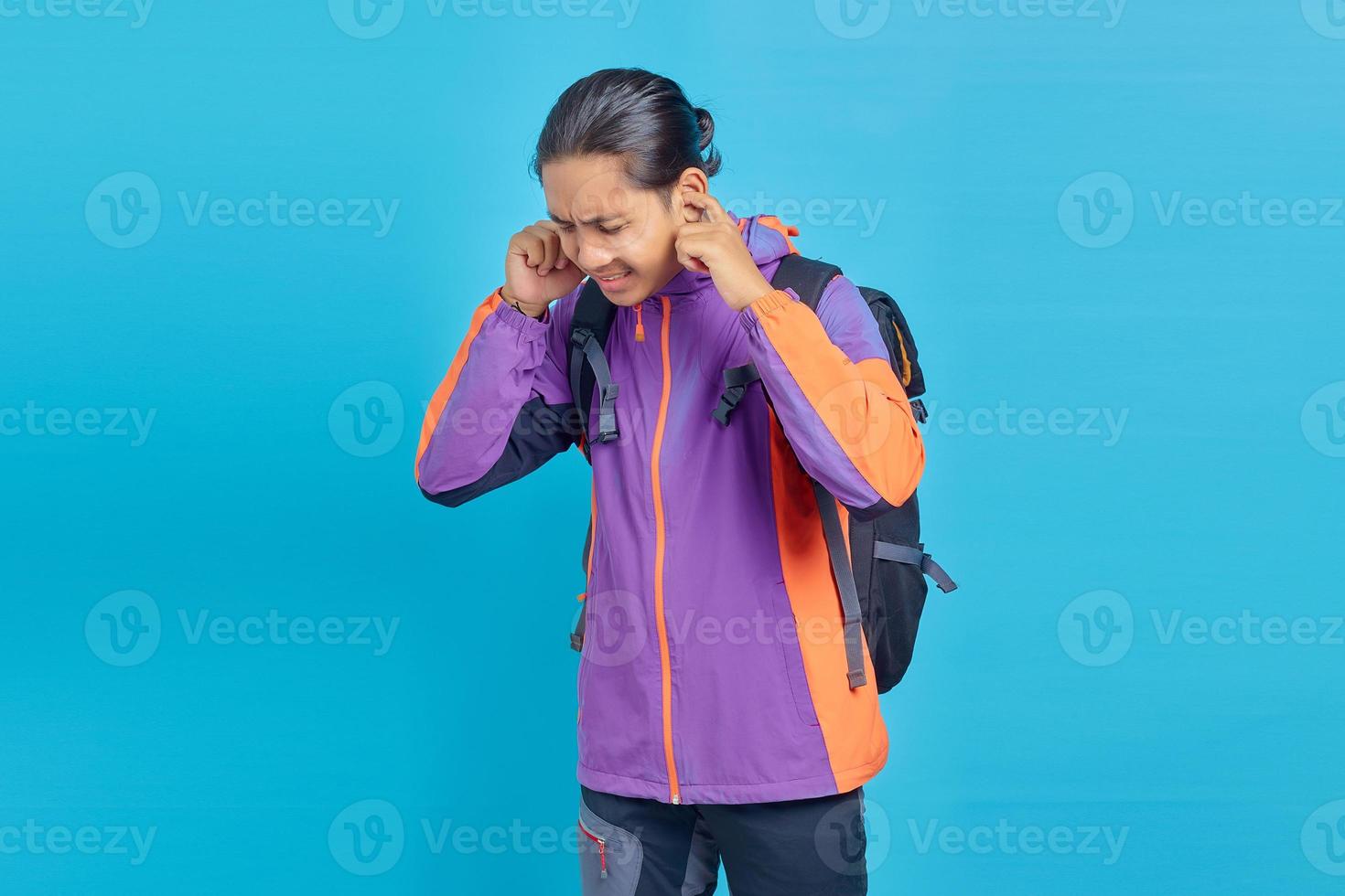 Handsome frustrated young man covering ears with angry expression on blue background photo