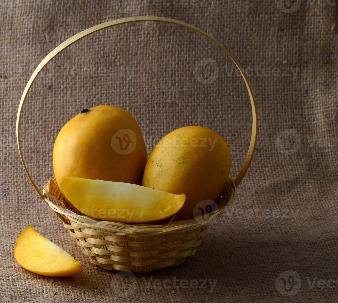 Fruta de mango en la canasta sobre fondo de tela de saco foto