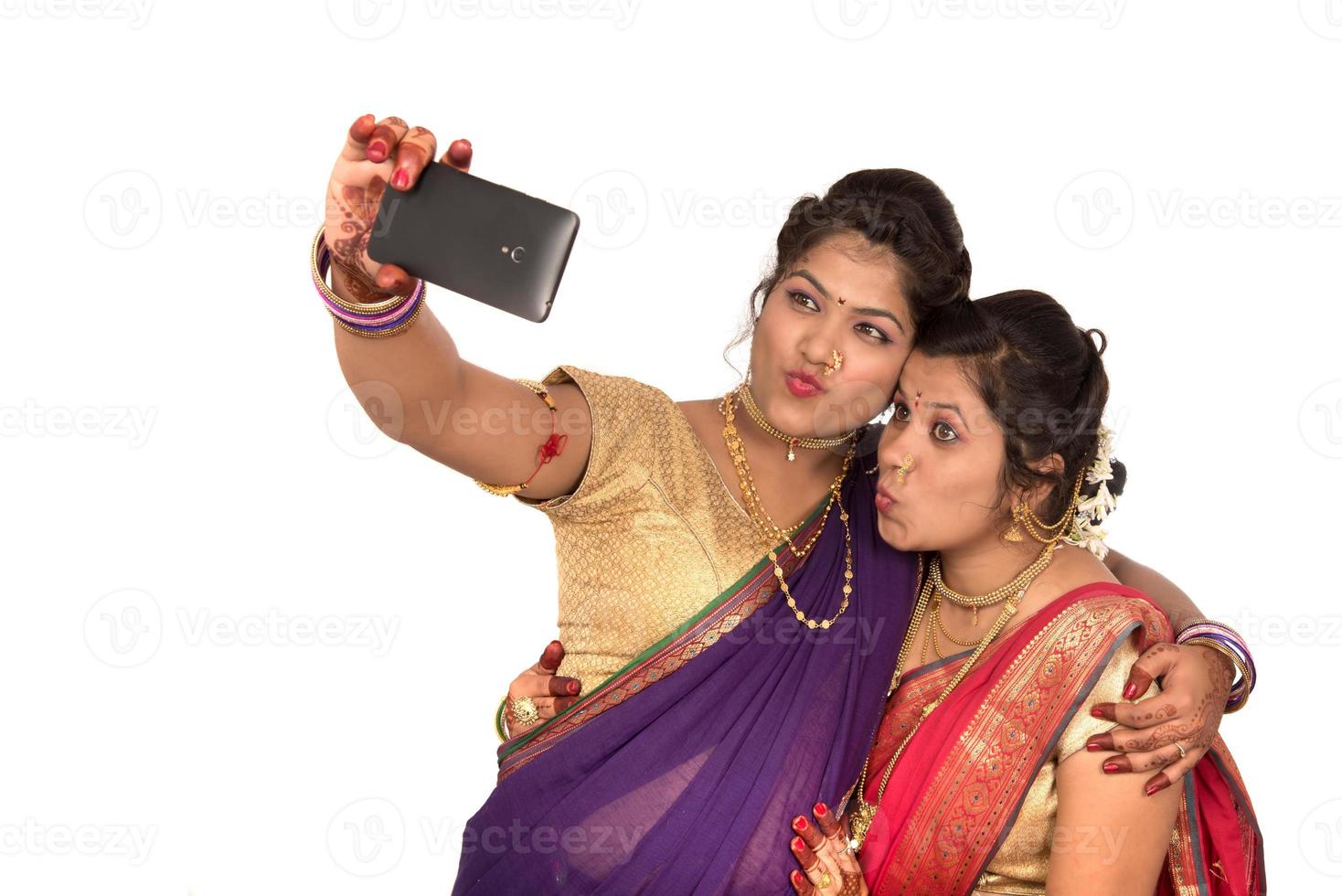Las niñas tradicionales indias tomando selfie con smartphone sobre fondo blanco. foto