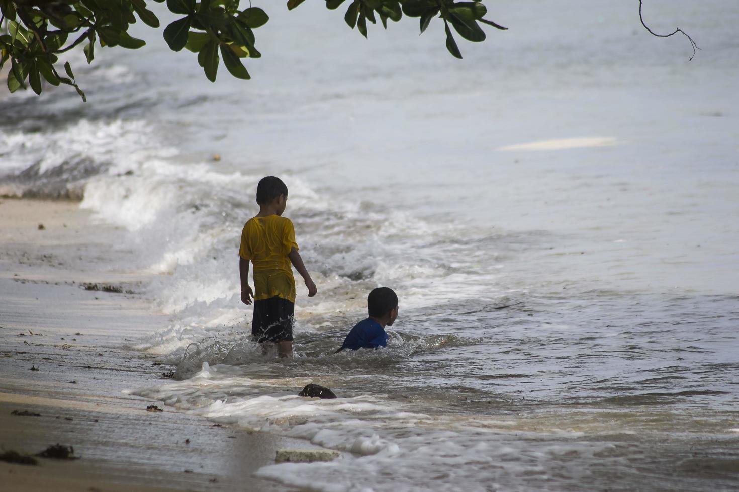 Sorong, West Papua, Indonesia, December 12th 2021. Boys playing against the waves on the beach photo
