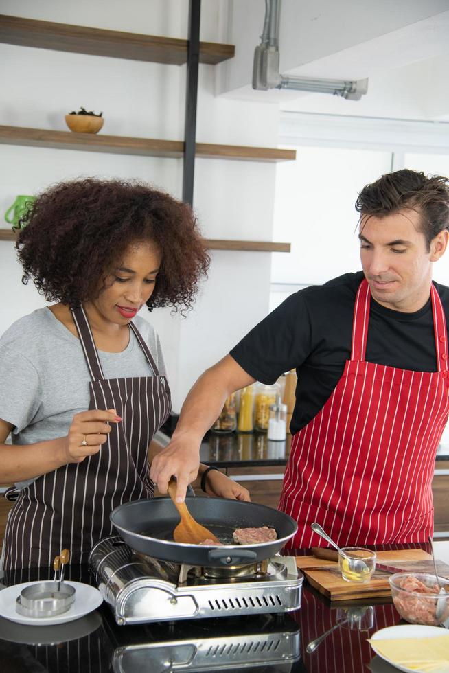 Pareja joven está alimentando mientras cocina una hamburguesa en la cocina foto