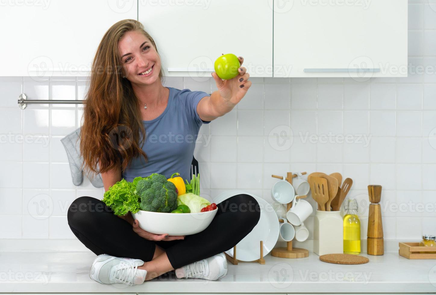 Foto sincera de joven mujer deportiva caucásica sentada en coutner en la cocina y comiendo un desayuno orgánico y saludable. concepto de autocuidado