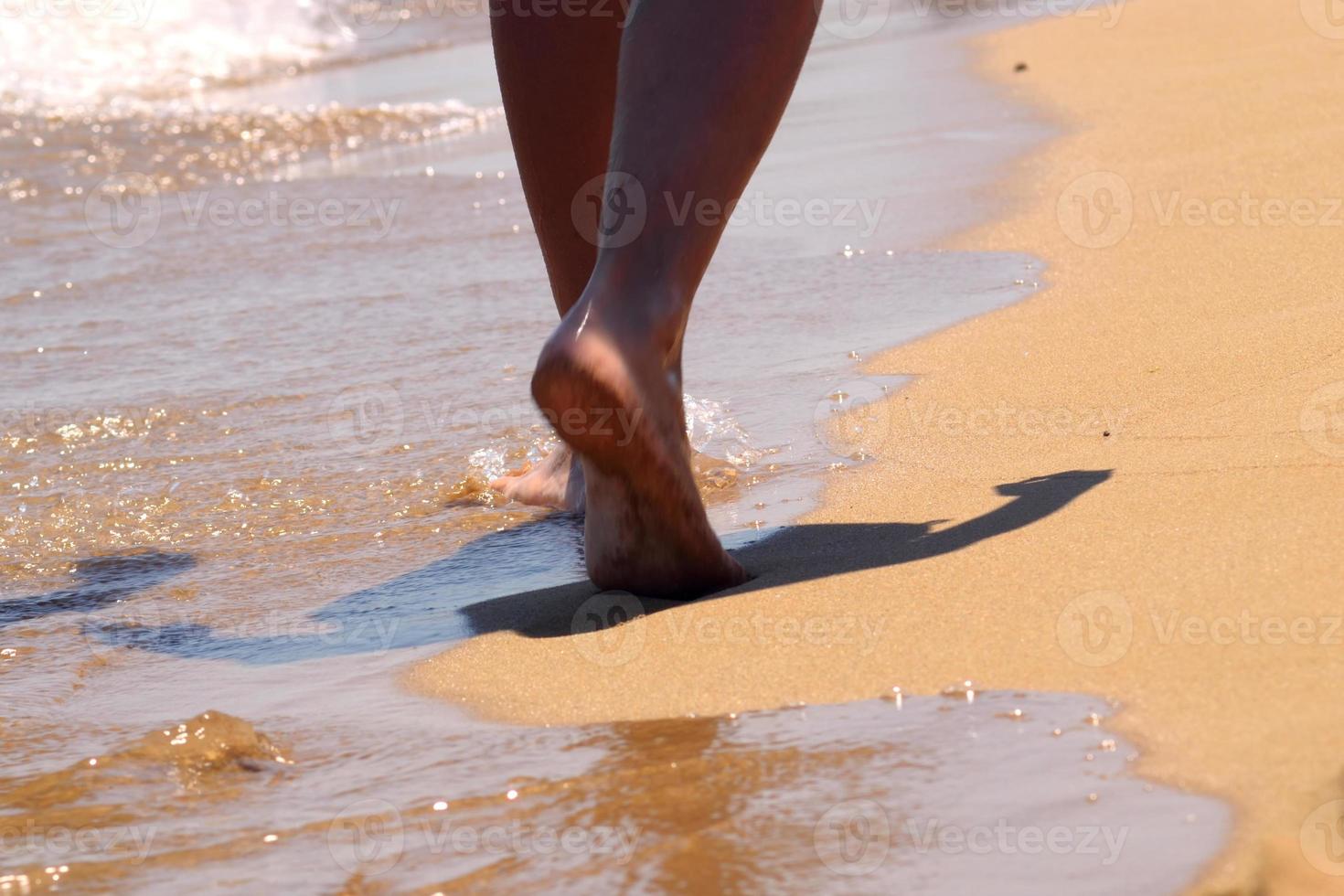 Woman walking barefoot on the sand leaving footprints on the golden beach. Female legs walk by the sea. Concept of vacation, summer vacation or vacation. photo