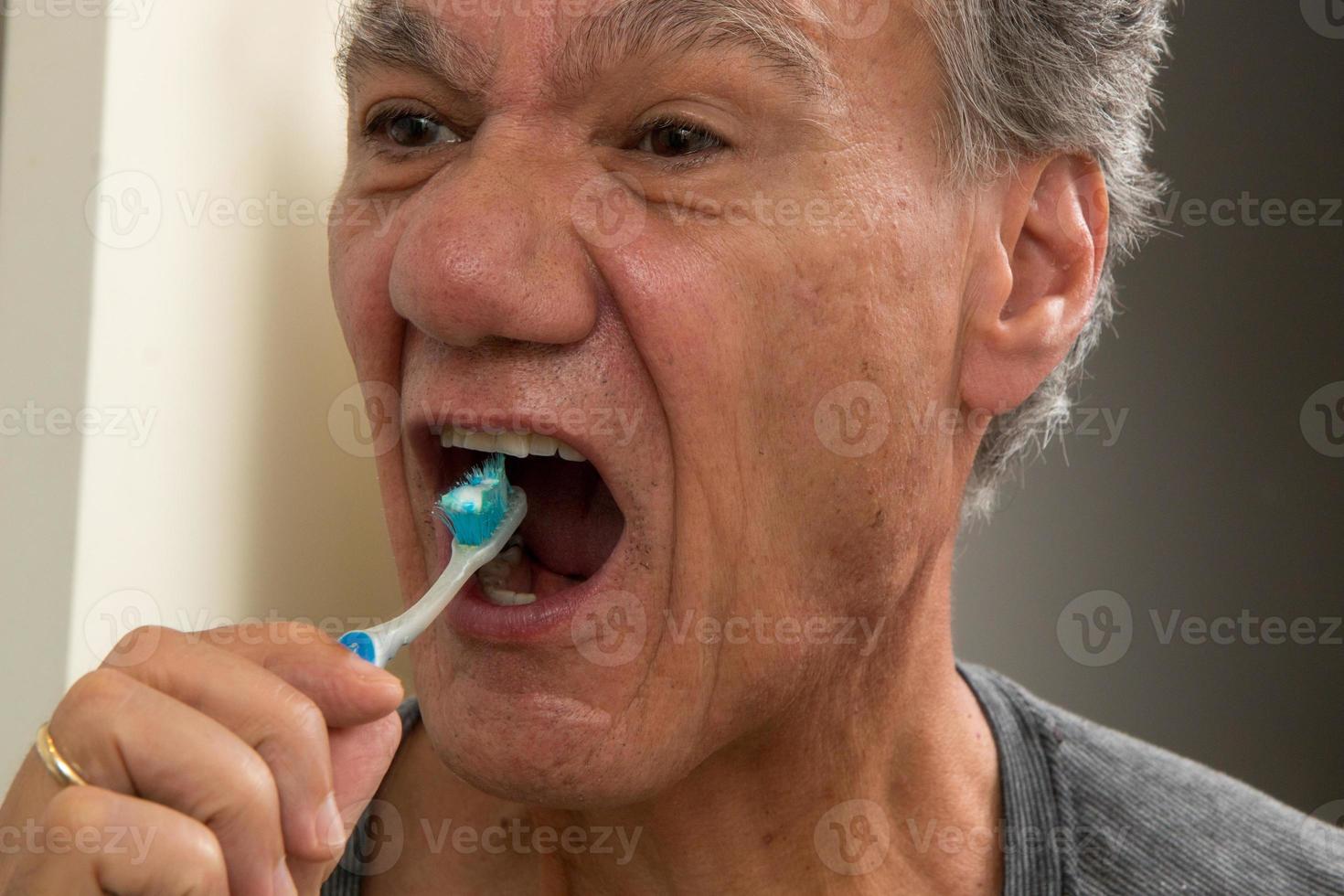 Mature Man Brushing his teeth with a Worn out Tooth Brush photo