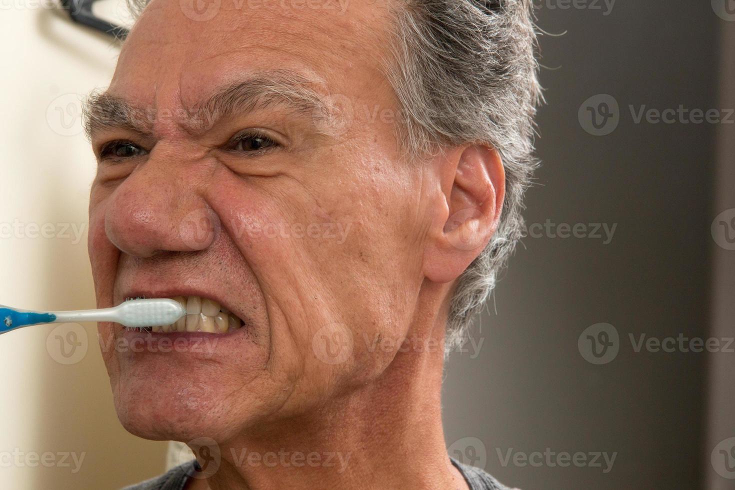 Mature Man Brushing his teeth with a Worn out Tooth Brush photo