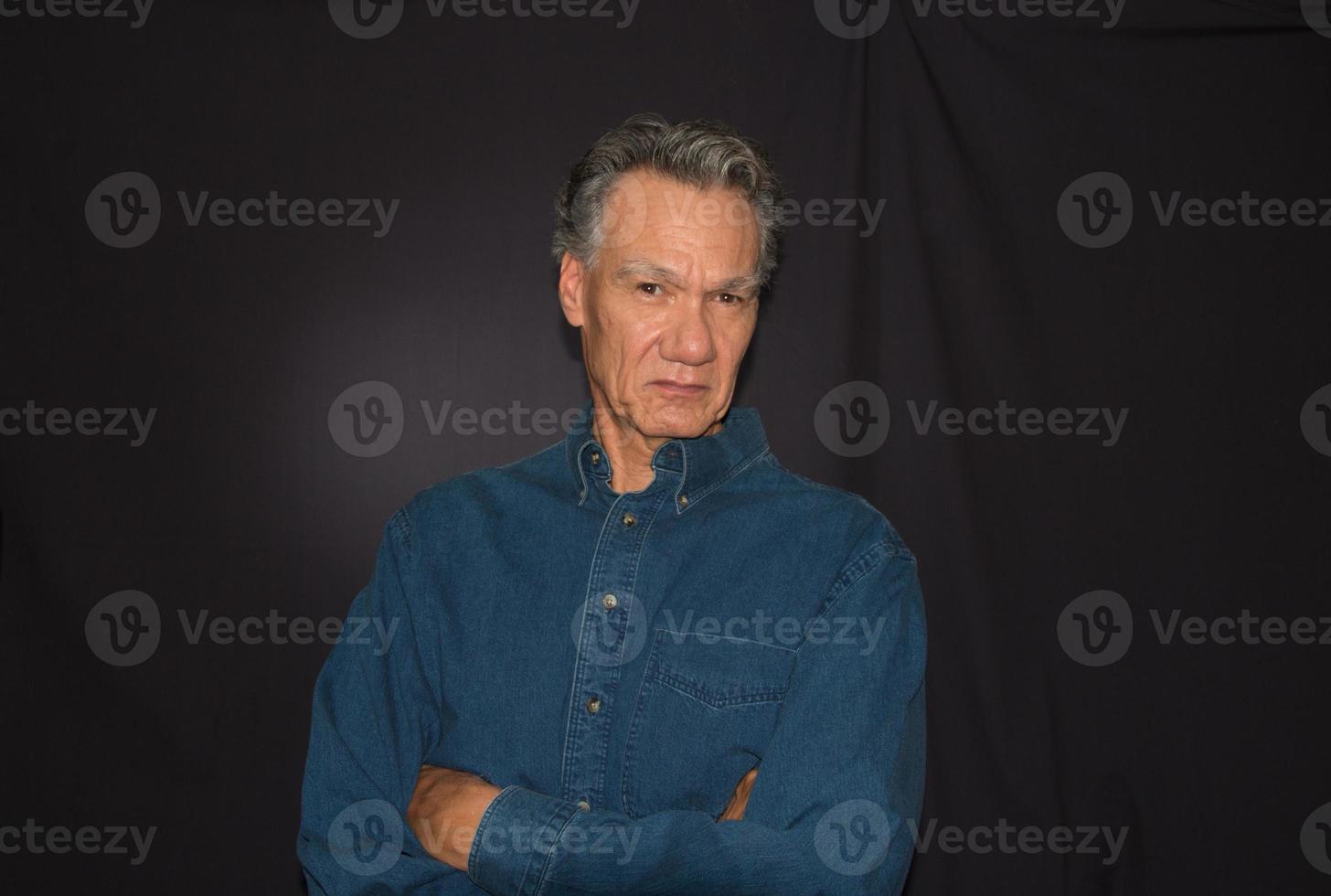 Dramatic Portrait of a Mature Man against a Black Background wearing a Denim Shirt photo