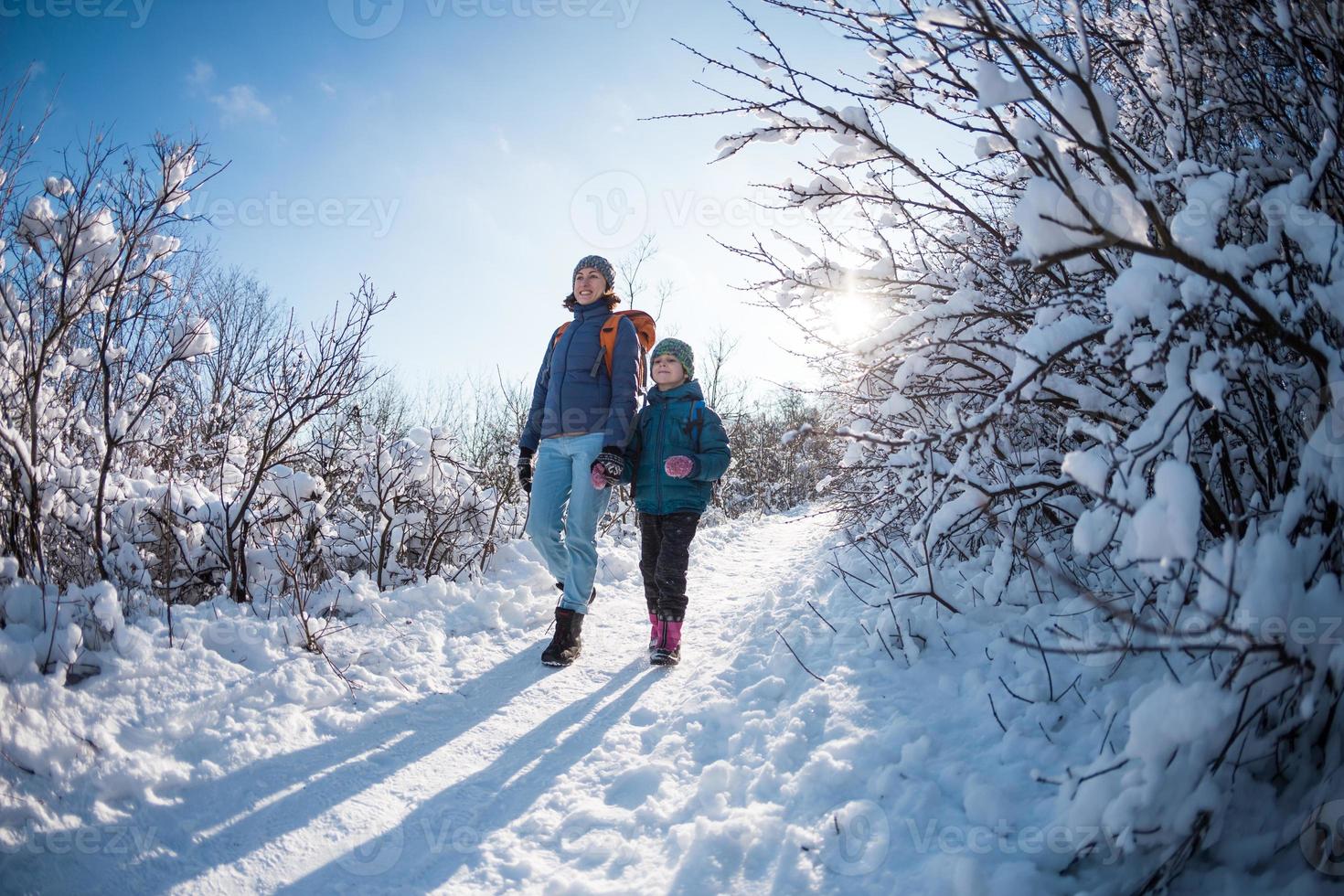 A child with a backpack walks with mother in a snowy forest photo