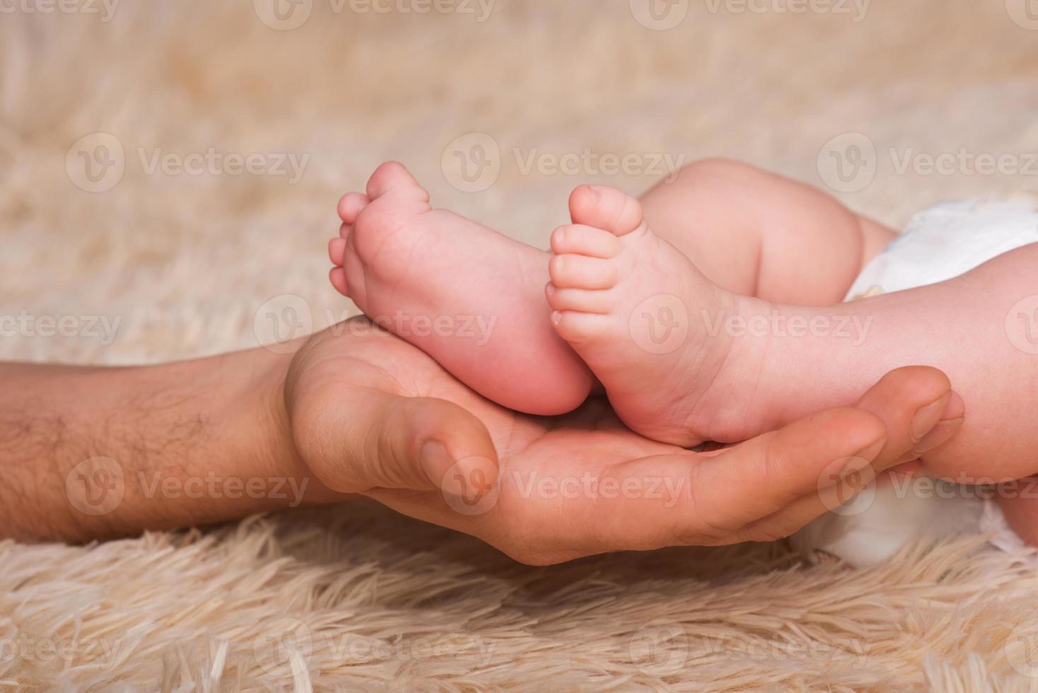 papá sostiene en sus manos un pequeño bebé pisa. piernas pequeñas de un bebé recién nacido en manos grandes de papá. masaje de pies de bebe foto