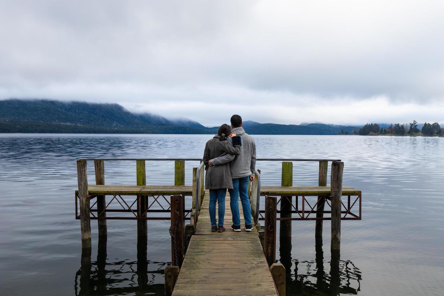 Young Asian couple hugging leaning on shoulder on the bridge Lake Te Anau New Zealand photo