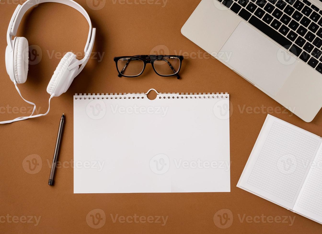 Top view desktop blank calendar, headphones and laptop on light brown background photo