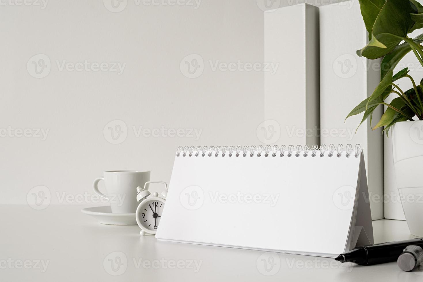 Mock up blank spiral calendar with flipping sheets on white table with coffee, stationery and clock photo