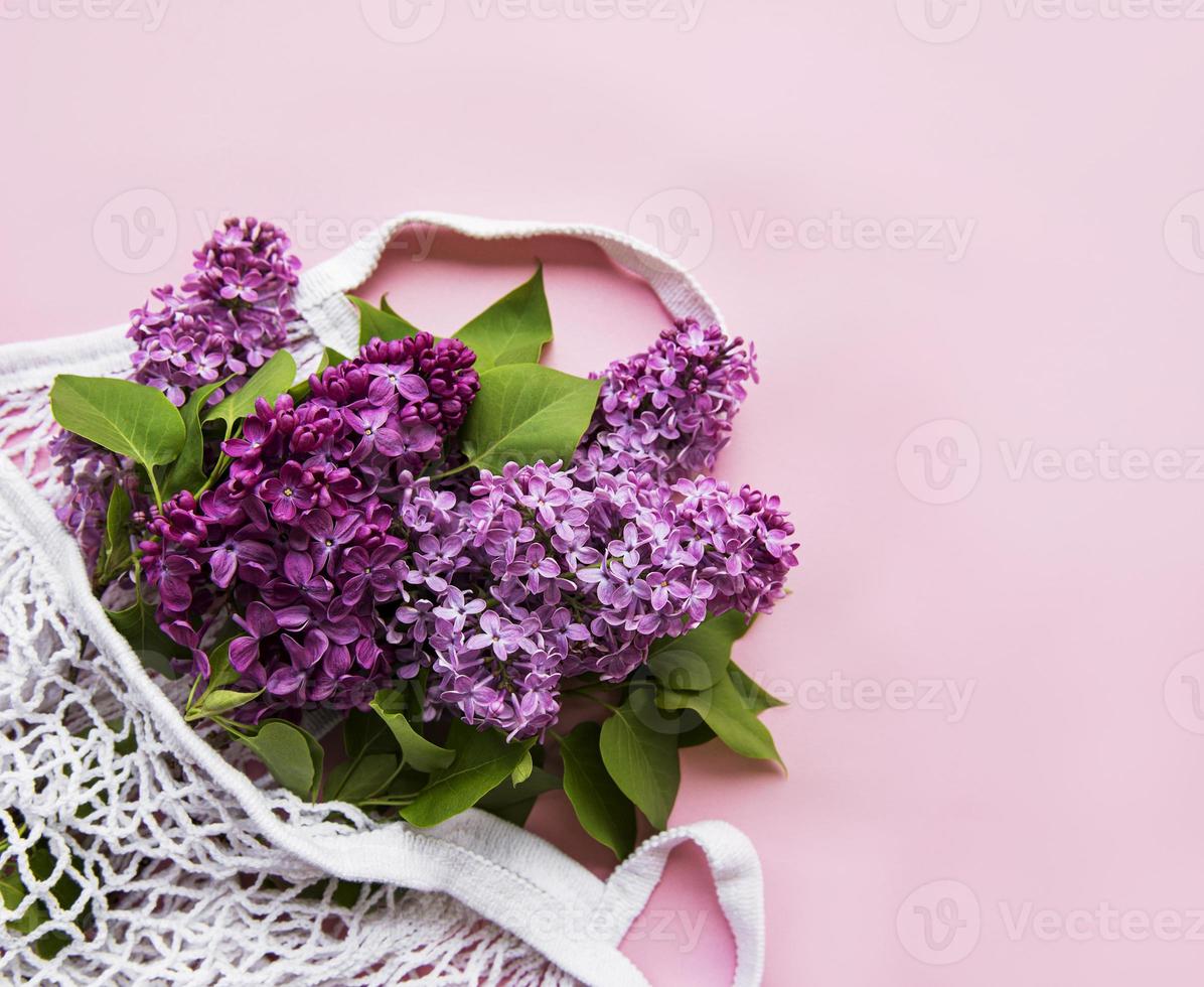 Bouquet of lilac in reusable shopping eco mesh bag on pink background. Concept no plastic, zero waste. Copy space Top view Template for greeting card, postcard, invitation. photo