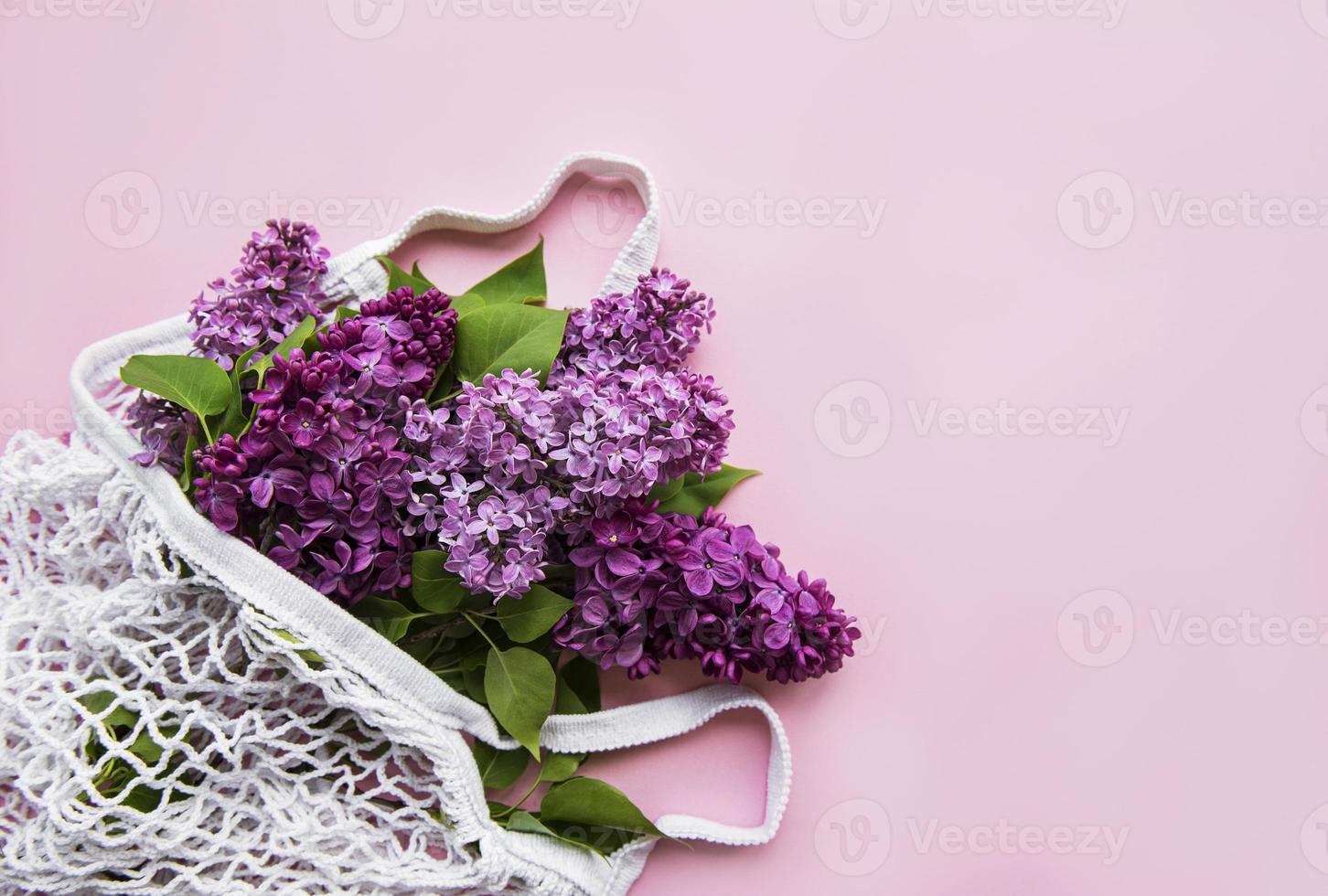 Bouquet of lilac in reusable shopping eco mesh bag on pink background. Concept no plastic, zero waste. Copy space Top view Template for greeting card, postcard, invitation. photo