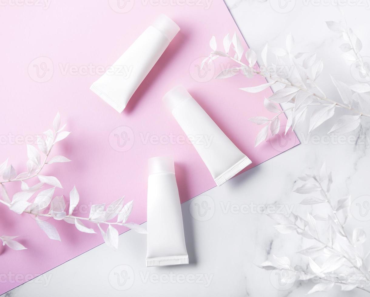 White tubes of cream on a marble and pink background photo