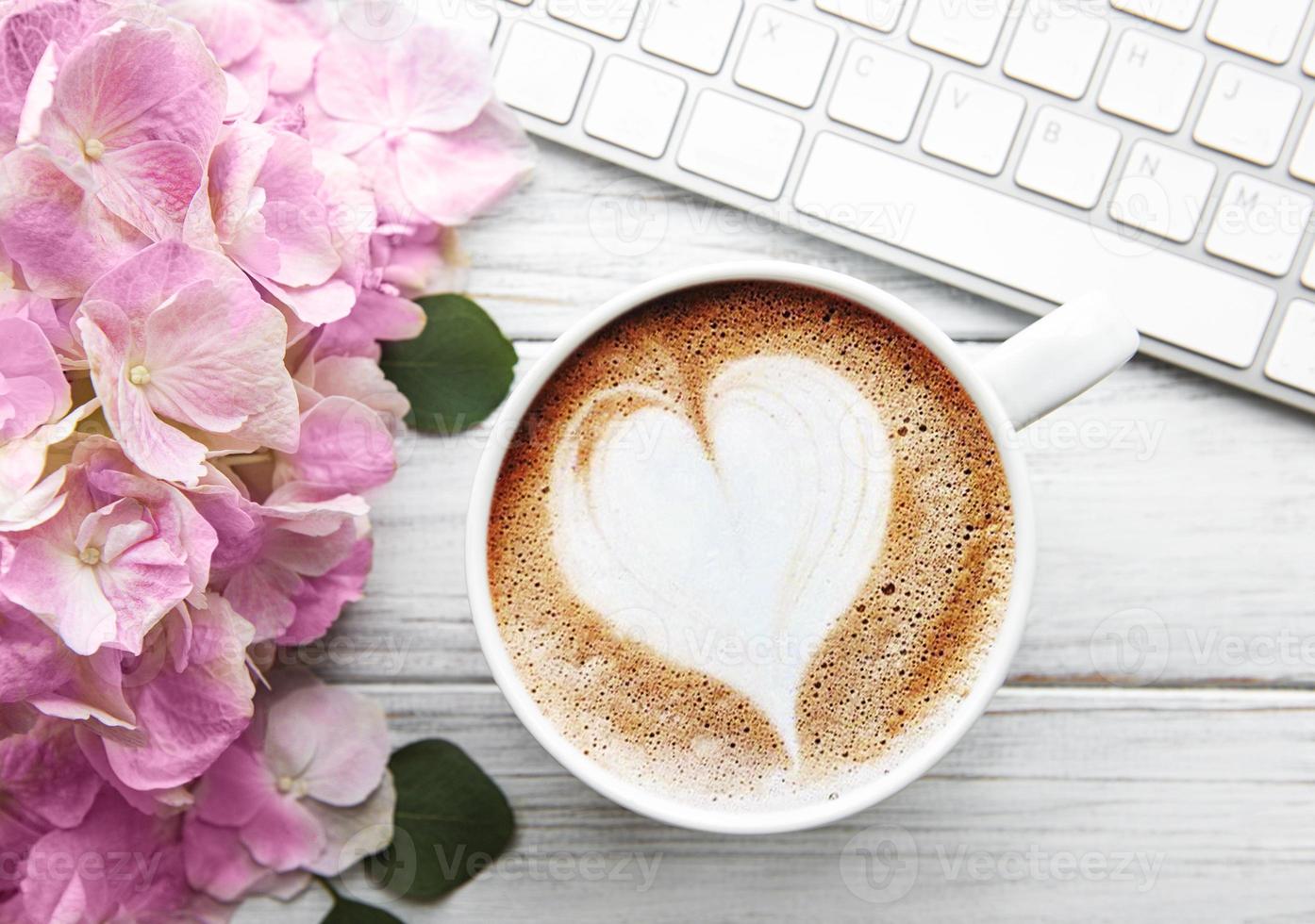 espacio de trabajo del escritorio de la oficina en casa con ramo de flores de hortensia rosa, taza de café y teclado foto