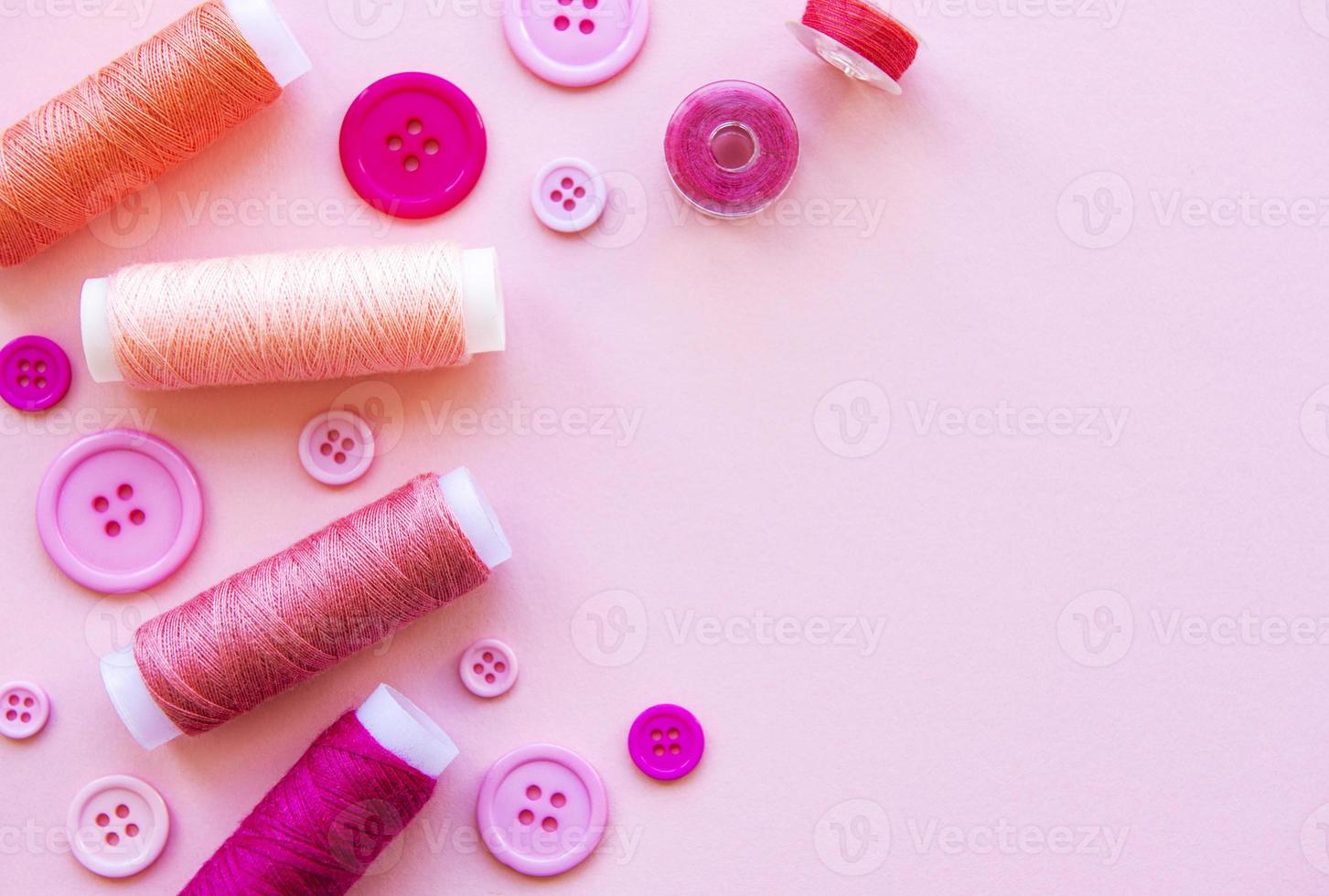Spools of thread and buttons in pink tones on a pink background photo