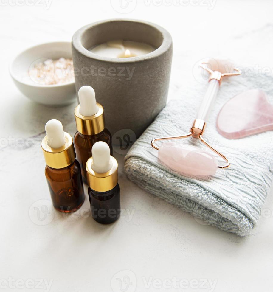 Face massage jade roller with cosmetic product on white marble background photo