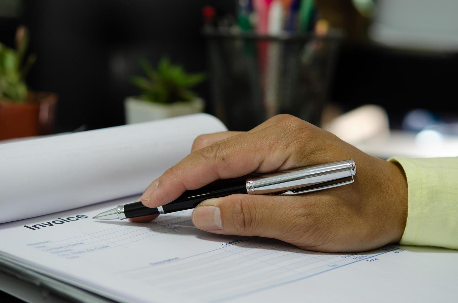 empresario mano sujetando la pluma en el documento de facturación de marketing y finanzas empresariales. foto