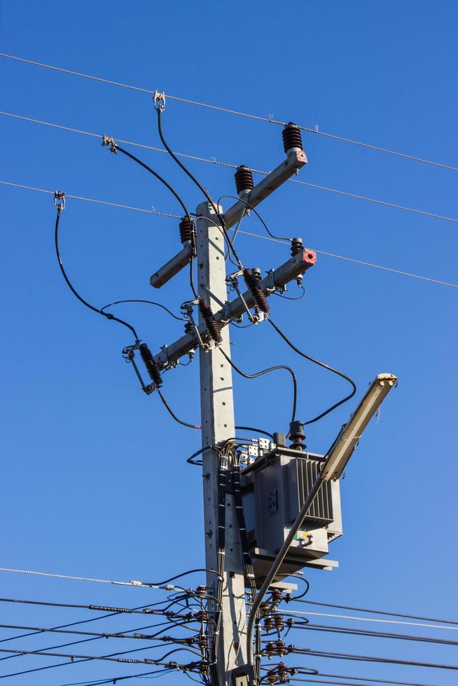Poste eléctrico conéctese a los cables eléctricos de alta tensión contra el cielo azul brillante foto