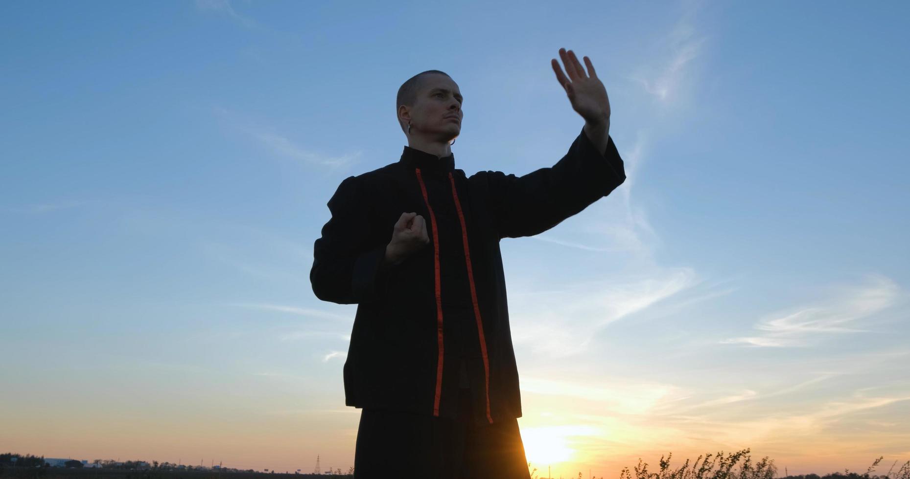 Silueta de joven luchador de kung fu practicando solo en los campos durante la puesta de sol foto