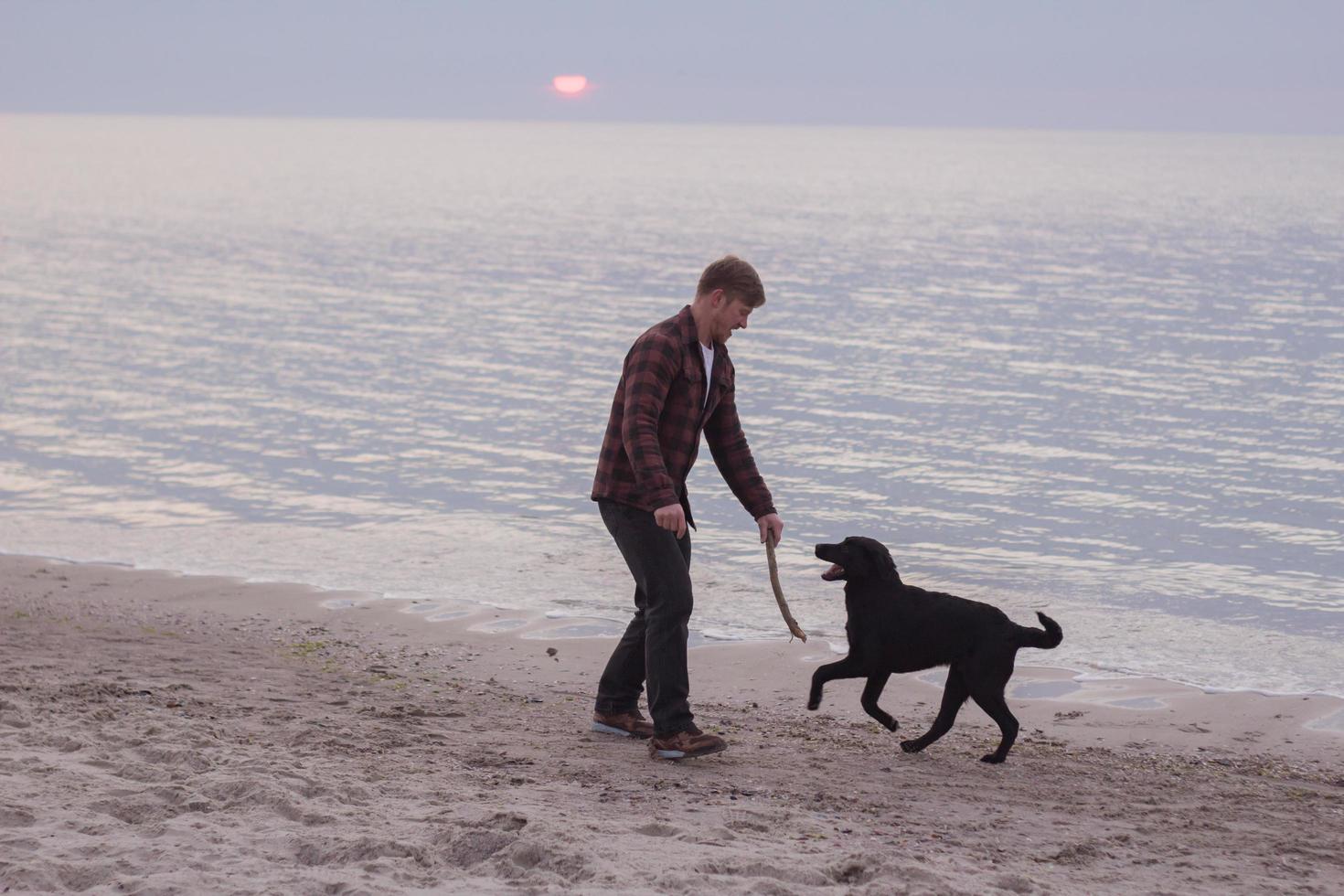 Joven caminando por la playa por la mañana con perro negro foto