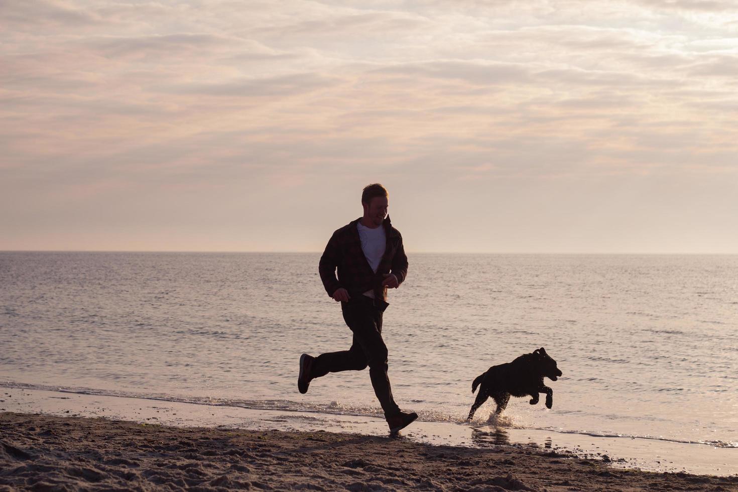 Joven caminando por la playa por la mañana con perro negro foto