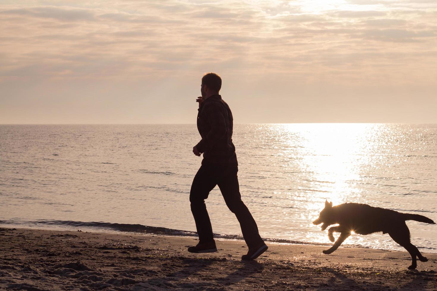 Joven caminando por la playa por la mañana con perro negro foto