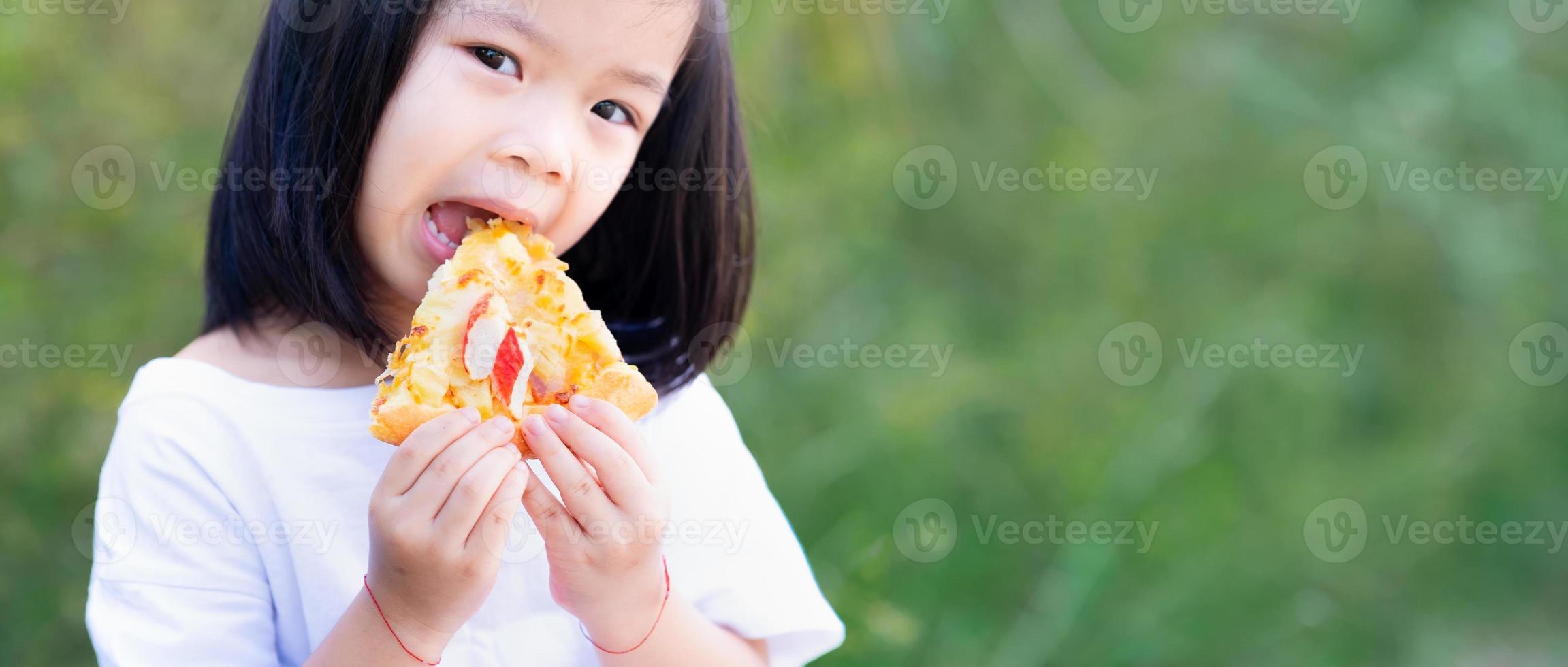 La mano del niño sostiene una deliciosa pizza. niño niña está feliz de comer comida. espacio vacío para ingresar texto. foto
