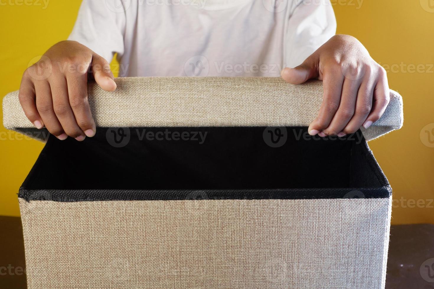 mano joven, sujete una caja contra el fondo amarillo foto