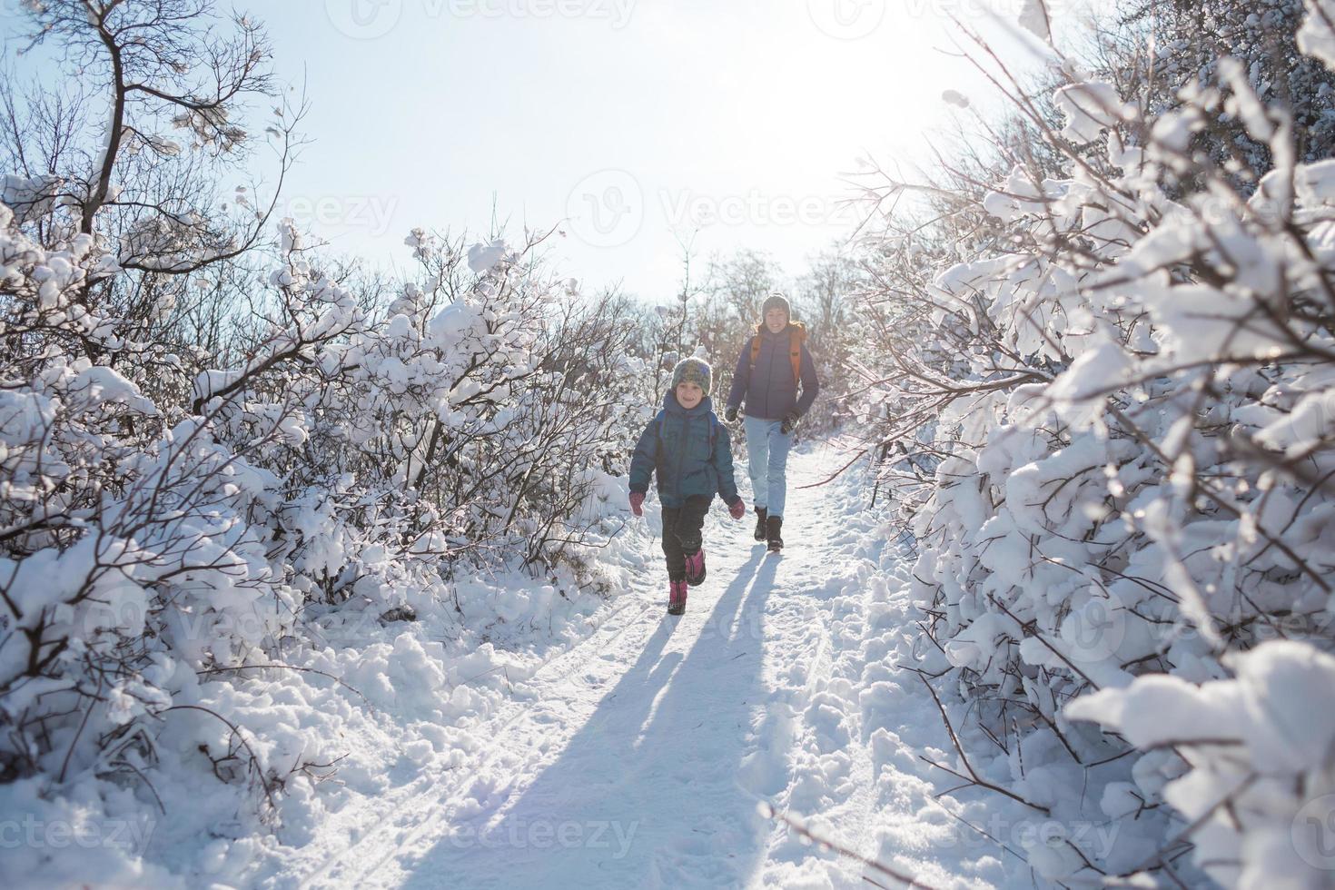 A child with a backpack walks with mother in a snowy forest photo