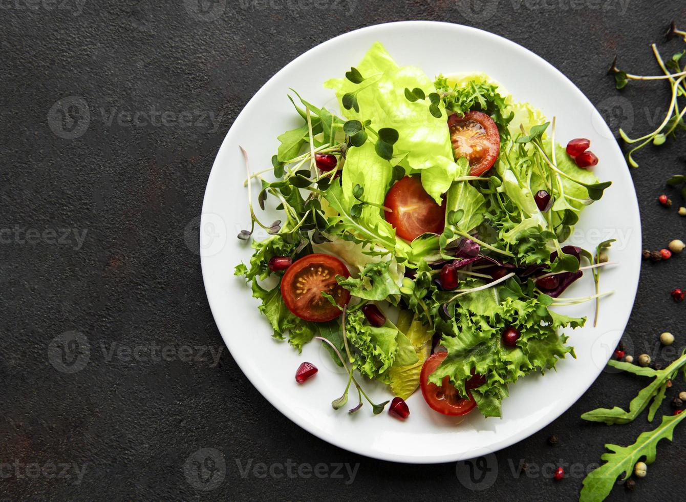 Fresh green mixed  salad bowl with tomatoes and microgreens  on black concrete background. Healthy food, top view. photo