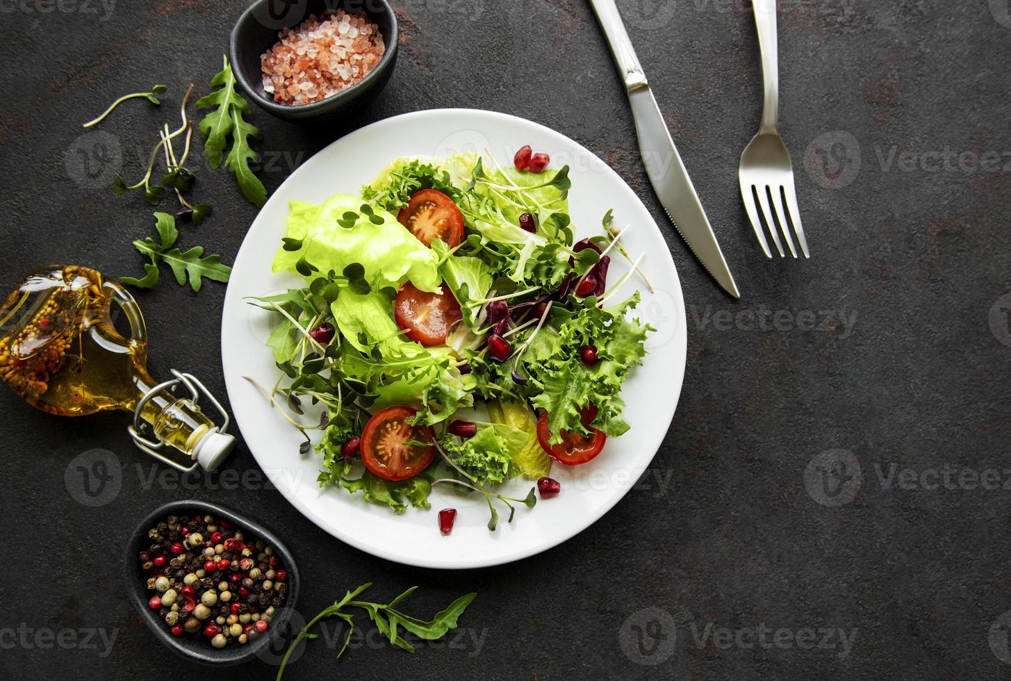 Fresh green mixed  salad bowl with tomatoes and microgreens  on black concrete background. Healthy food, top view. photo