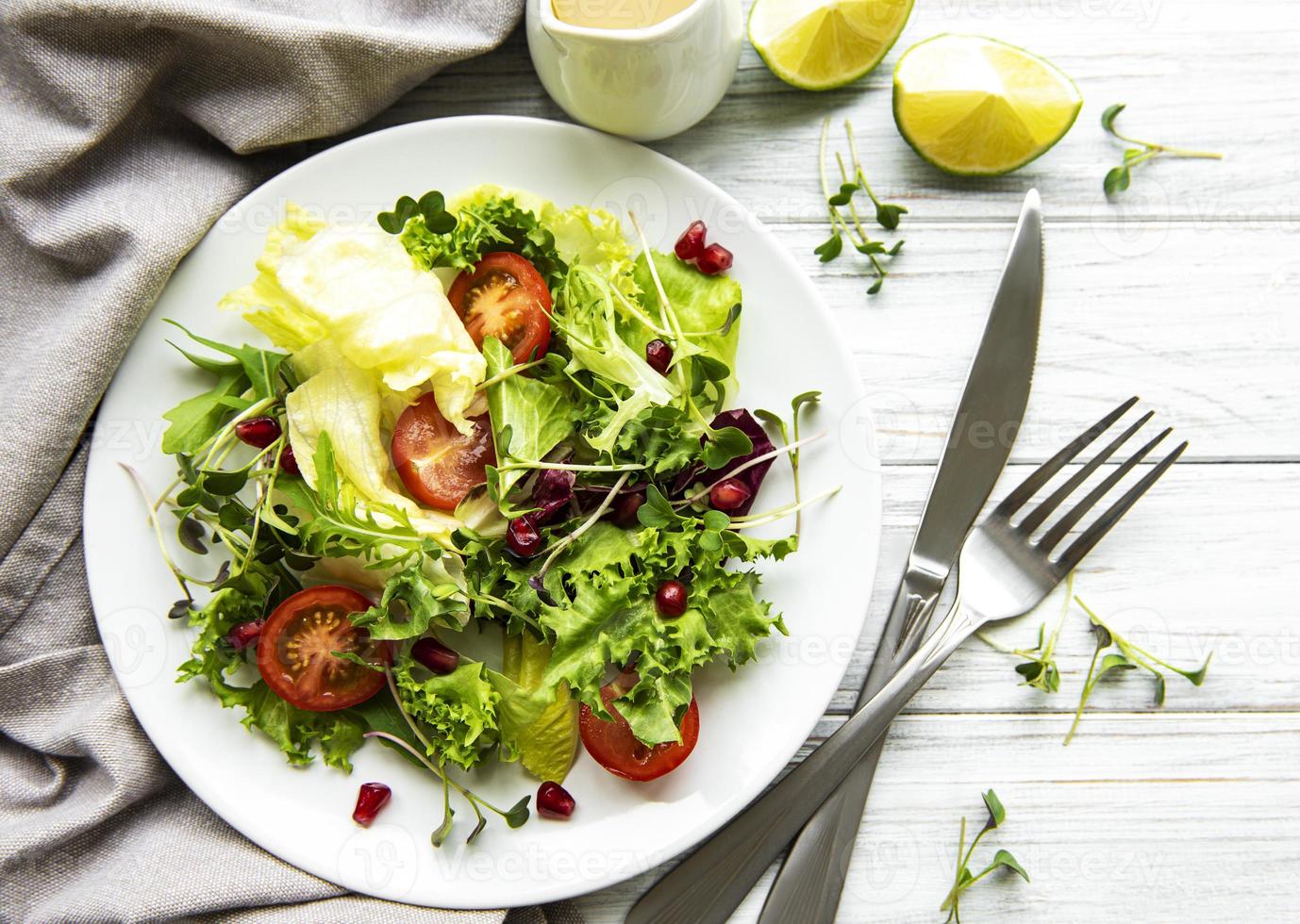 Fresh green mixed  salad bowl with tomatoes and microgreens  on white wooden background. Healthy food, top view. photo