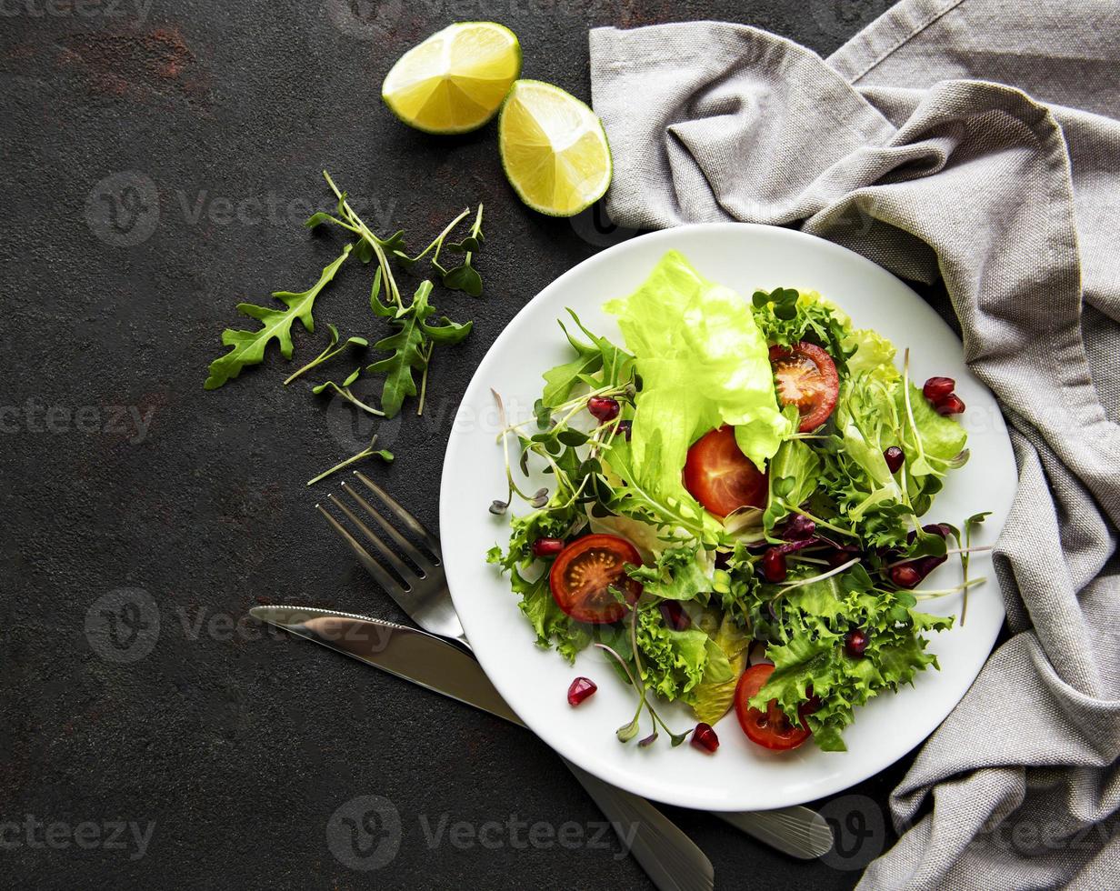 Fresh green mixed  salad bowl with tomatoes and microgreens  on black concrete background. Healthy food, top view. photo