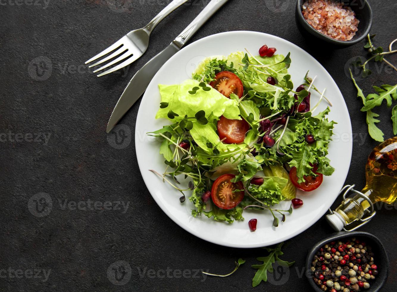 Ensaladera mixta verde fresca con tomates y microgreens sobre fondo de hormigón negro. comida sana, vista superior. foto