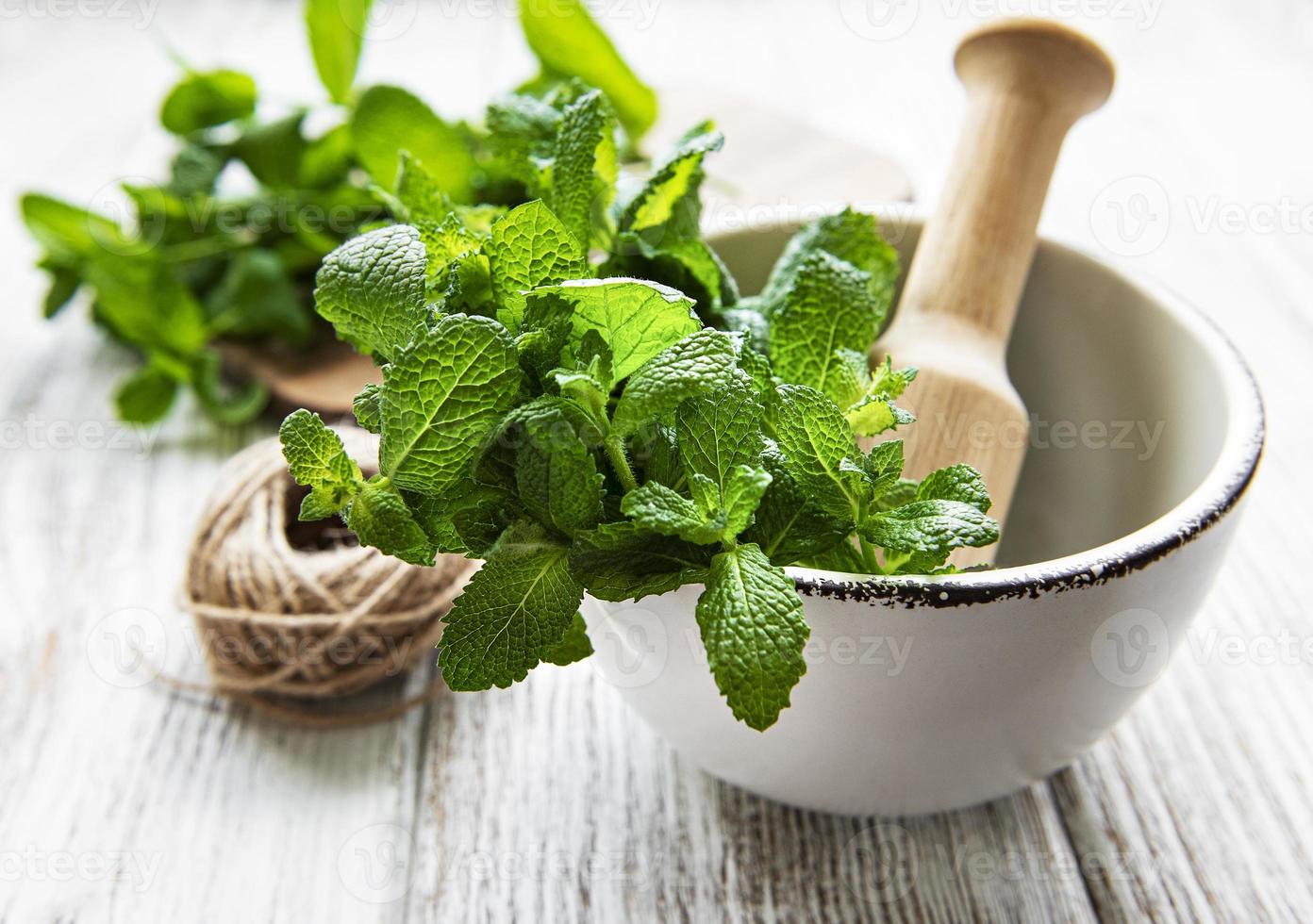 Fresh green mint in mortar on white wooden background photo